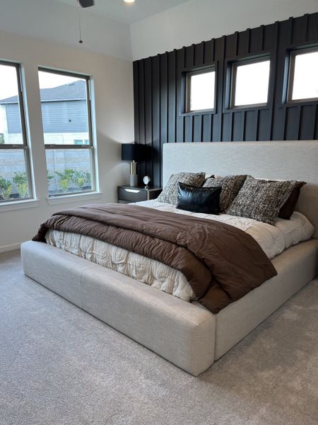 A cozy bedroom with a plush upholstered bed, textured accent wall, and large windows letting in ample natural light. A cozy bedroom with a plush upholstered bed, textured accent wall, and large windows letting in ample natural light.