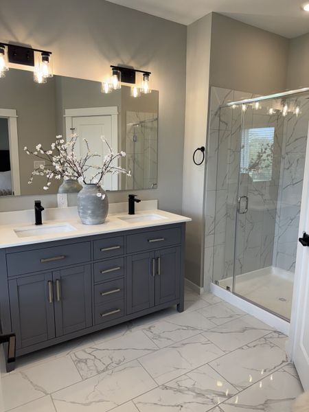 A modern bathroom featuring a sleek gray vanity, elegant lighting, and a spacious glass-enclosed marble shower.