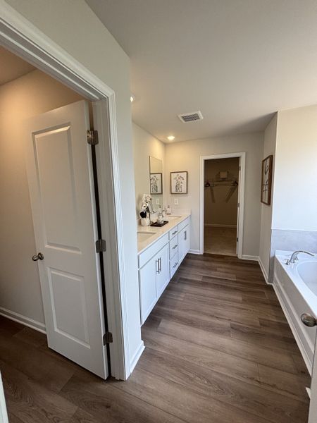 A spacious bathroom featuring a sleek double vanity, wood-style flooring, and a luxurious bathtub.