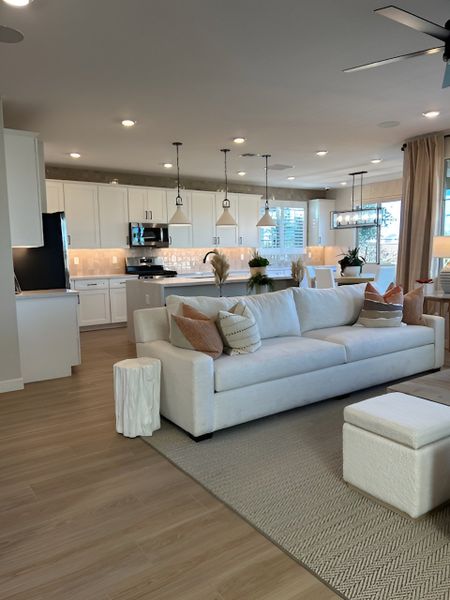 A modern kitchen with white cabinetry, pendant lighting, and a spacious island adjacent to the living area.