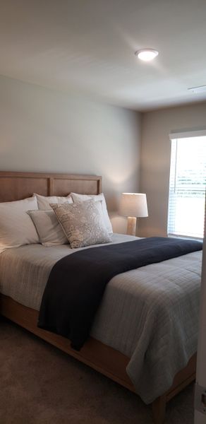 A cozy bedroom featuring a plush bed, elegant neutral tones, and a softly lit lamp for a serene ambiance.
