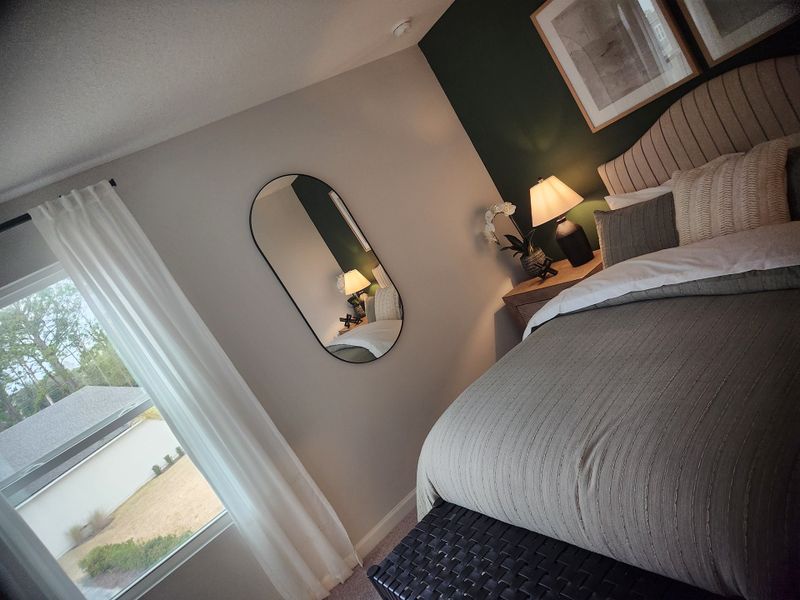A cozy bedroom with a textured grey bedspread, dark accent wall, stylish mirror, and soft lighting for a serene ambiance.