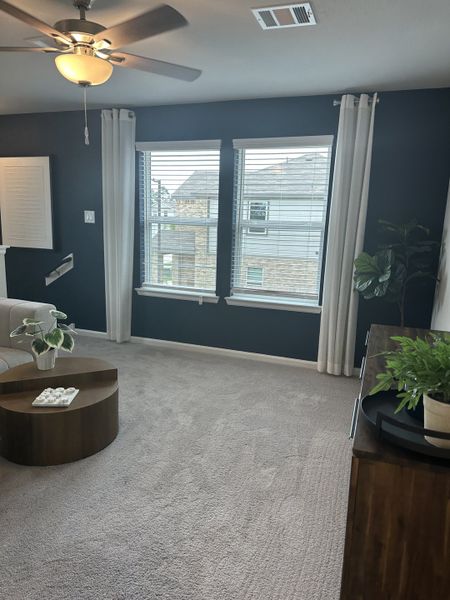 A cozy living area with plush carpeting, dark accent wall, ceiling fan, and natural light from large windows. A cozy living area with plush carpeting, dark accent wall, ceiling fan, and natural light from large windows.
