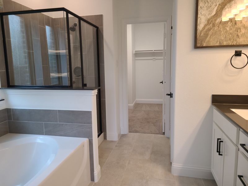 Sleek bathroom with a spacious tub, glass shower, gray tiles, and modern vanity, leading to a walk-in closet. Sleek bathroom with a spacious tub, glass shower, gray tiles, and modern vanity, leading to a walk-in closet.