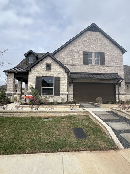 A charming stone and brick home with dark shutters and a manicured yard in Ladera Prosper by Ladera Texas (Prosper, TX). A charming stone and brick home with dark shutters and a manicured yard in Ladera Prosper by Ladera Texas (Prosper, TX).