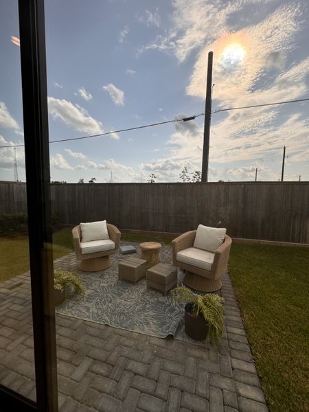 Cozy patio with wicker chairs, a patterned rug, and greenery, perfect for relaxing outdoors.