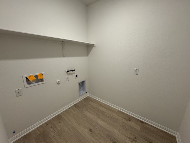 A laundry room with wood flooring, white walls, and shelving space, designed for practicality and organization.