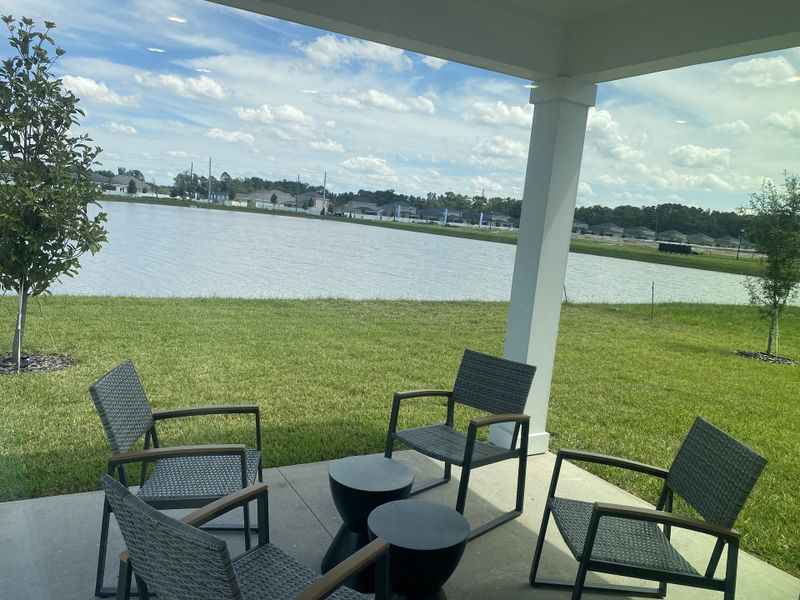 A tranquil patio area overlooking a serene lake, with modern outdoor seating on a lush green lawn.