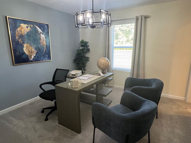 A cozy home office with modern art, plush seating, elegant chandelier, and a sleek desk with a globe.