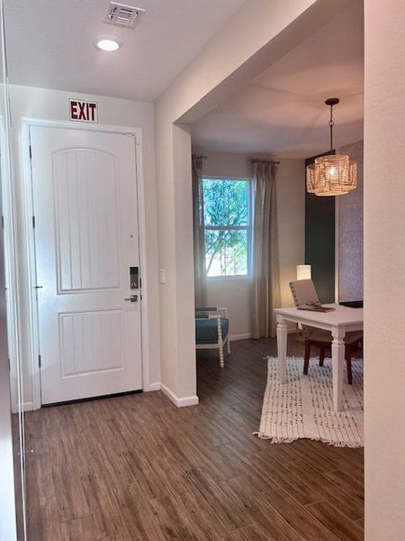 A cozy entryway with wood flooring, leading to a well-lit office space featuring a stylish pendant light and window view.