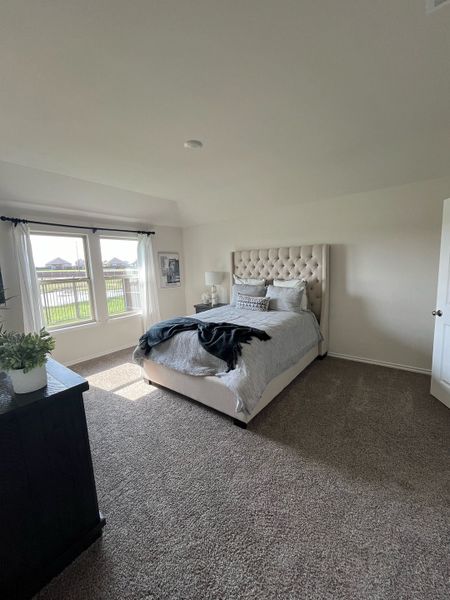 Cozy bedroom featuring a plush bed, soft carpeting, and ample natural light through large windows.