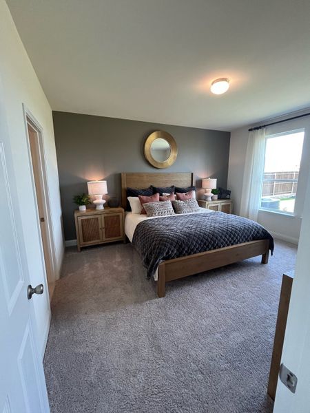 A cozy bedroom featuring a warm, wooden bed, soft carpeting, and natural light filtering through large windows.