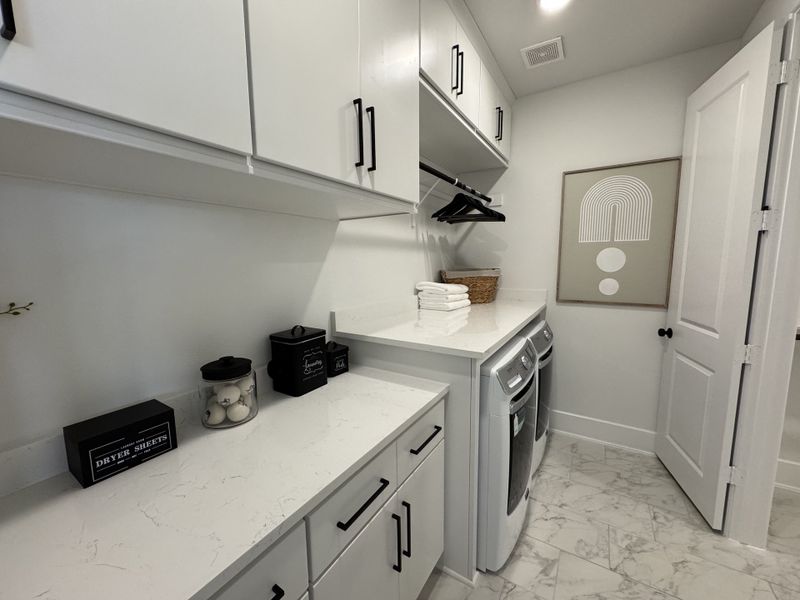 A sleek laundry room featuring white cabinetry, marble countertops, and modern appliances. Clean, minimalistic design.