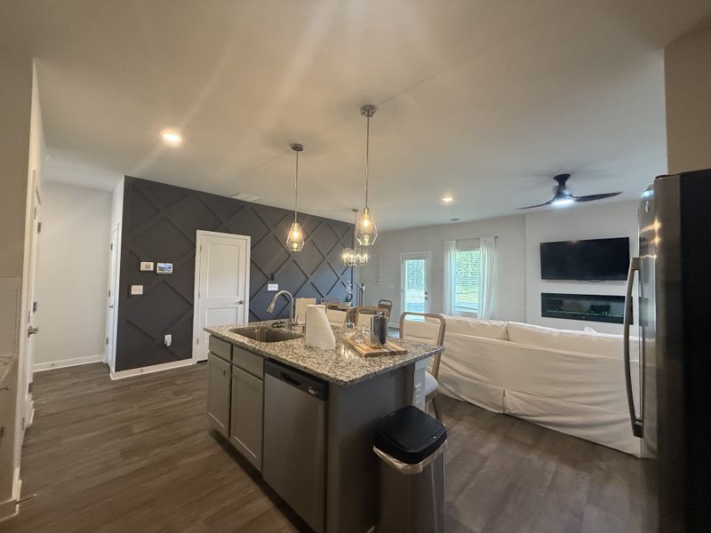 Modern kitchen with granite island, pendant lighting, and a cozy living area, featuring a sleek fireplace and TV. Modern kitchen with granite island, pendant lighting, and a cozy living area, featuring a sleek fireplace and TV.