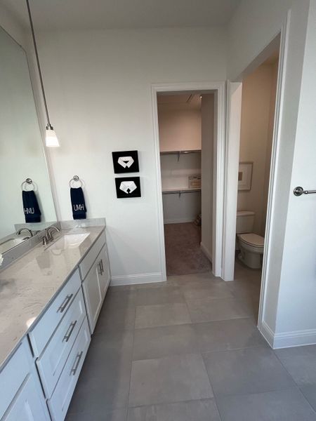 A modern bathroom with sleek white cabinetry, pendant lighting, and access to a spacious walk-in closet.
