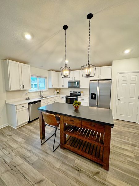 A modern kitchen featuring sleek white cabinets, stainless steel appliances, and chic pendant lighting over a wooden island.