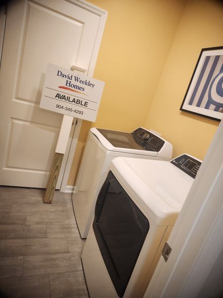 A cozy laundry room featuring modern appliances, warm yellow walls, and sleek wood flooring.