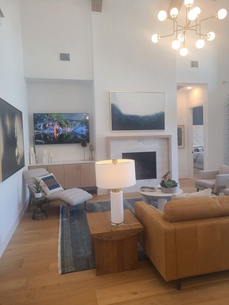 A cozy living room featuring a modern chandelier, tan sofa, TV, abstract art, and a chaise lounge with sleek decor.