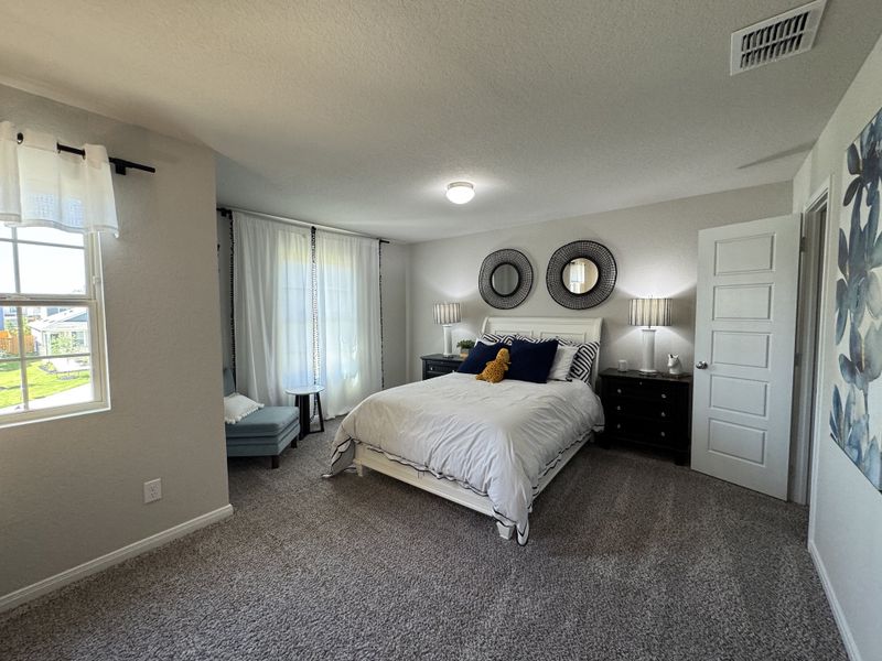 A cozy bedroom with plush carpet, elegant bedside lamps, and soft natural light filtering through large windows.