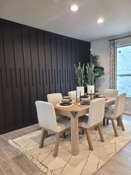 A chic dining area with a wooden table, upholstered chairs, and a bold dark accent wall for modern elegance.