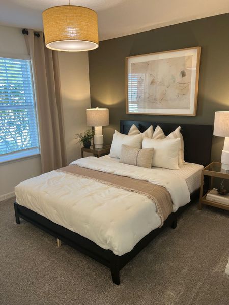 A cozy bedroom with a stylish pendant light, taupe curtains, and a plush bed with neutral accents.
