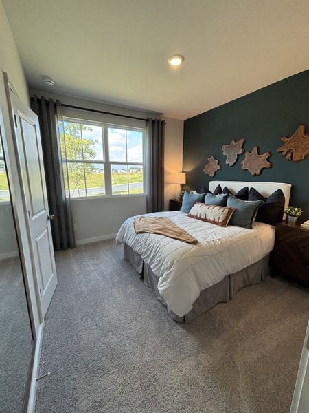 A cozy bedroom with dark accent wall, stylish art pieces, and large window illuminating a comfy bed with plush pillows.