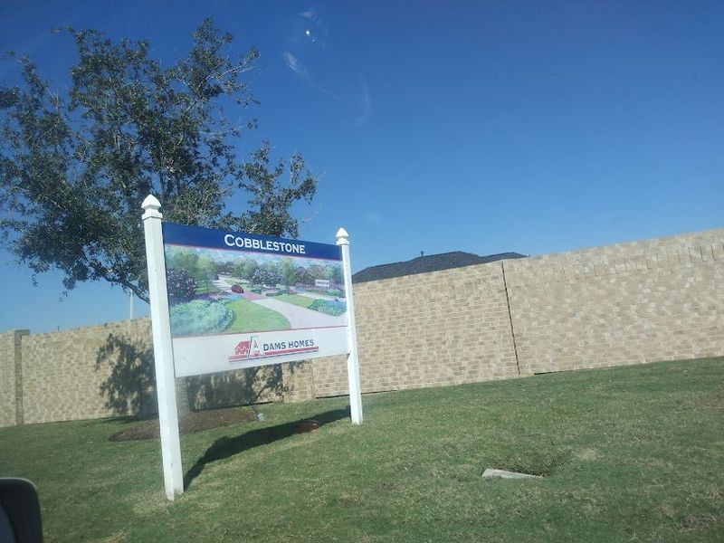 A grand entrance sign for Cobblestone by Adams Homes, showcasing a well-maintained community with lush green spaces.