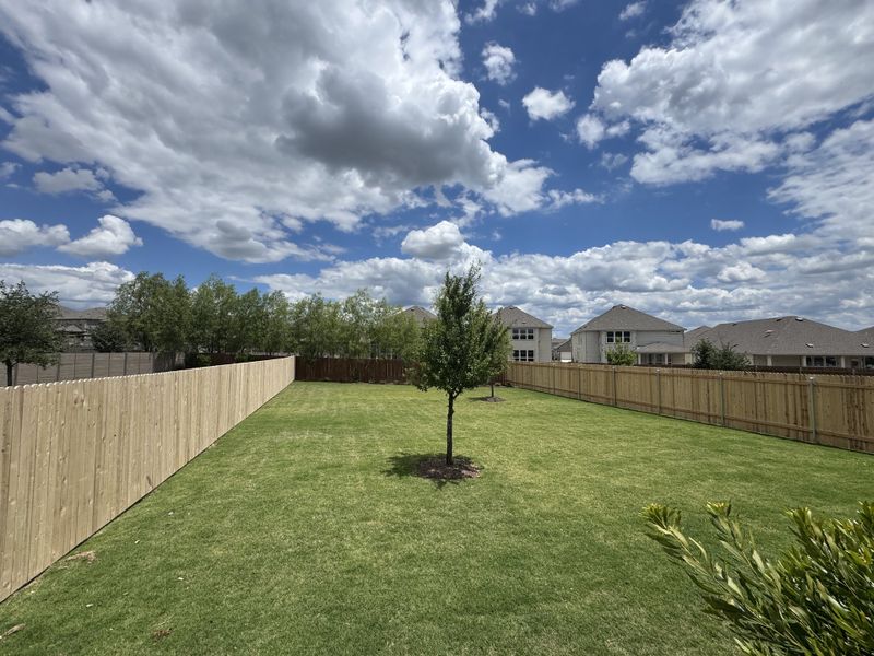 A spacious fenced backyard with lush greenery in McKinney Crossing by KB Home (Austin, TX).