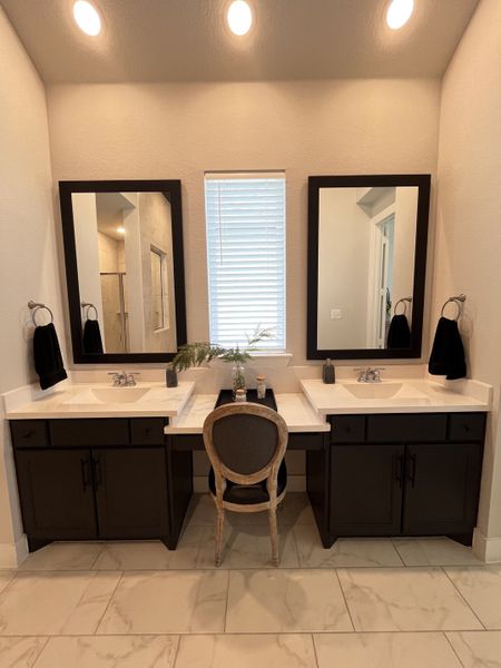 A chic bathroom with dual sinks, elegant mirrors, and a cozy chair on pristine tile flooring. A chic bathroom with dual sinks, elegant mirrors, and a cozy chair on pristine tile flooring.