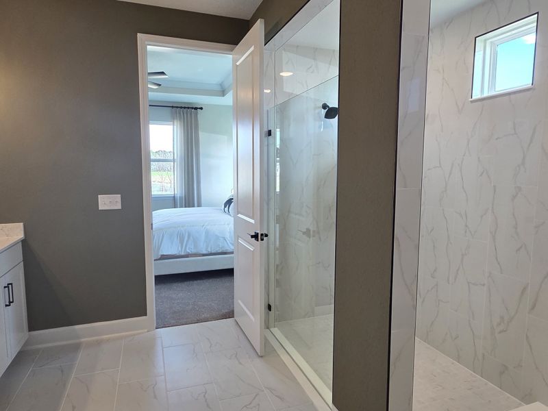 Elegant bathroom with a glass shower, modern tiles, and an open doorway to a cozy bedroom.