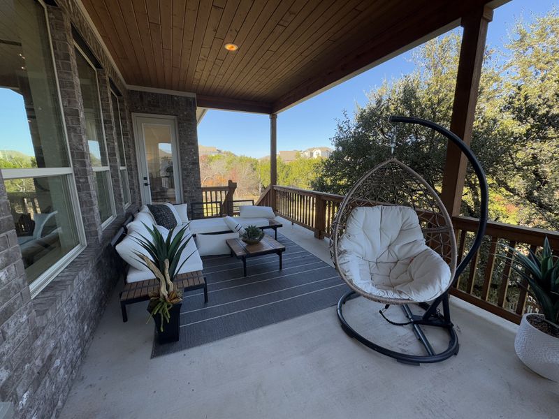 A cozy patio with white seating, hanging chair, and potted plants overlooking lush greenery under a wooden ceiling. A cozy patio with white seating, hanging chair, and potted plants overlooking lush greenery under a wooden ceiling.