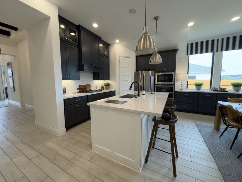 A sleek kitchen with dark cabinets, a white island, pendant lighting, and large windows.