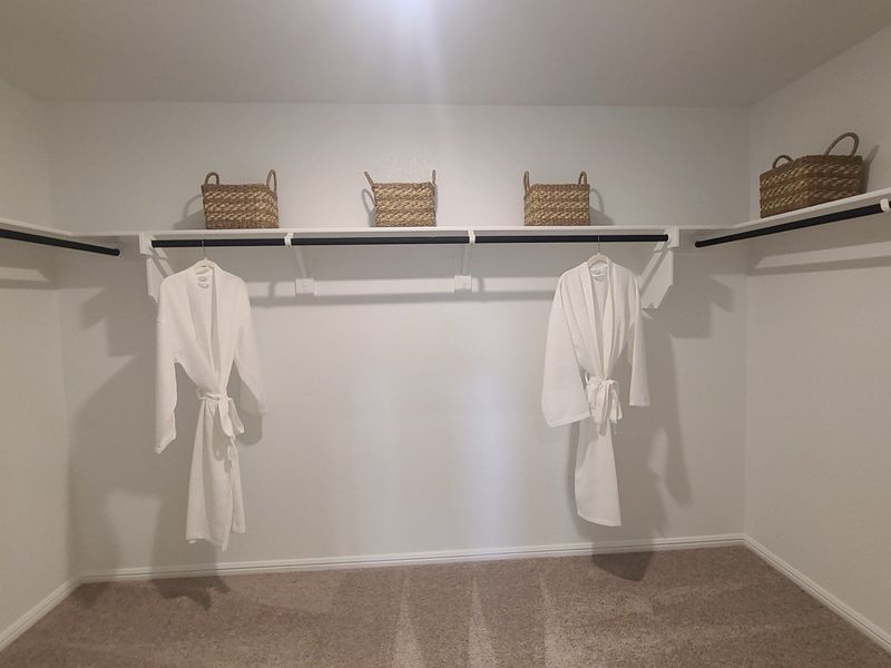 A spacious walk-in closet with cozy carpet, featuring baskets and plush white robes on elegant shelving. A spacious walk-in closet with cozy carpet, featuring baskets and plush white robes on elegant shelving.