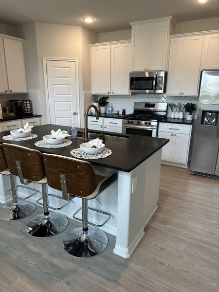 A modern kitchen with white cabinets, black countertops, stainless steel appliances, and chic barstools. Elegant and inviting space.