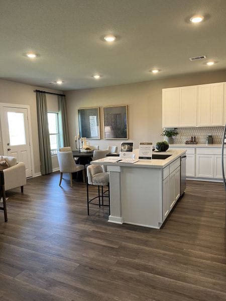 A contemporary kitchen and dining area with wood floors, white cabinets, and cozy seating in an open-concept layout.