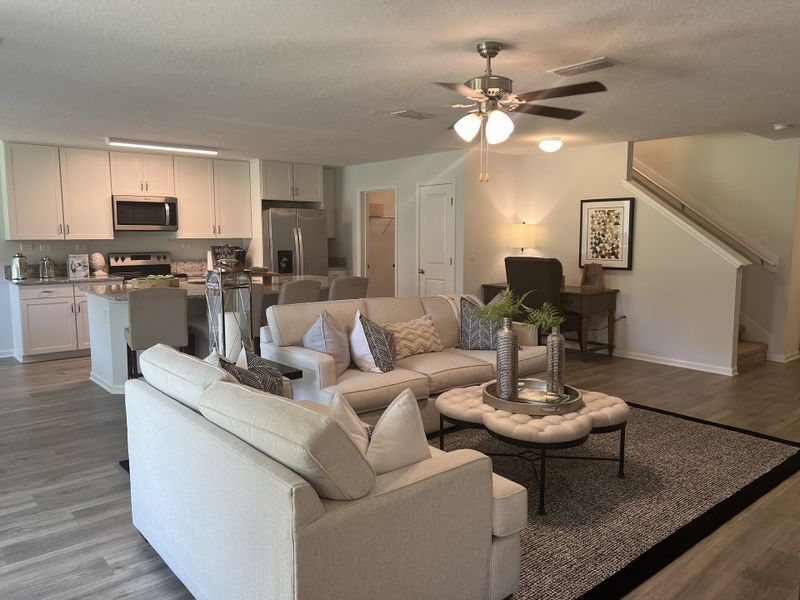 Open-concept living area with neutral-toned furniture, a cozy seating arrangement, and a modern kitchen in the background. Open-concept living area with neutral-toned furniture, a cozy seating arrangement, and a modern kitchen in the background.