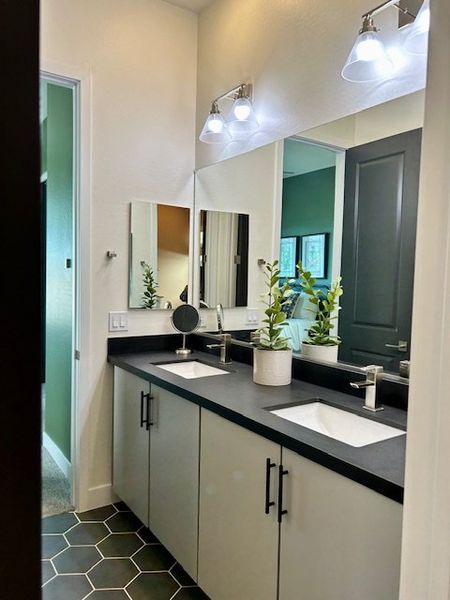 A sleek bathroom with dual sinks, black countertop, modern fixtures, and stylish lighting.