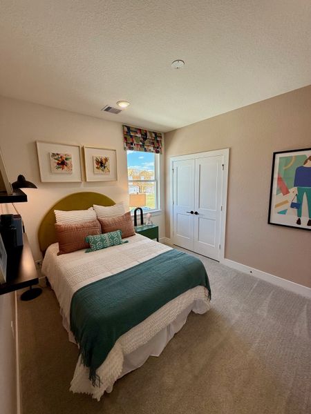A cozy bedroom features a modern bed with vibrant pillows, framed art, and a large window for natural light. A cozy bedroom features a modern bed with vibrant pillows, framed art, and a large window for natural light.