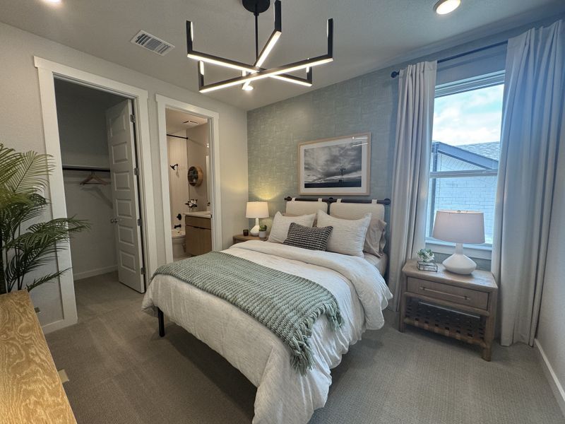 A cozy bedroom featuring a modern chandelier, soft bedding, and subtle decor with a serene atmosphere.