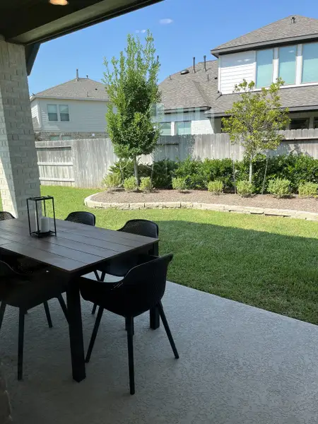 A cozy patio with a sleek dining set overlooks a landscaped yard and trees, perfect for outdoor gatherings.