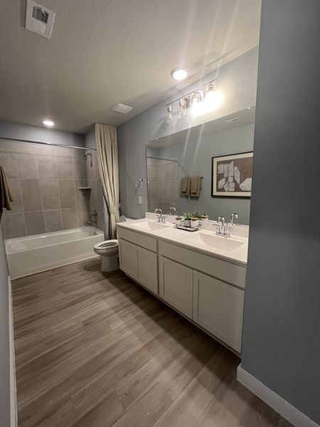 A modern bathroom featuring a spacious double vanity, sleek lighting, and a bathtub with gray tile surround. A modern bathroom featuring a spacious double vanity, sleek lighting, and a bathtub with gray tile surround.