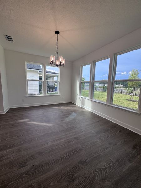 A bright dining area with large windows, dark wood floors, and a modern chandelier, offering serene exterior views.
