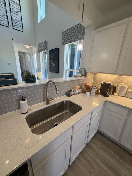 A modern kitchen featuring white cabinets, gray tile backsplash, and a sleek stainless steel sink.