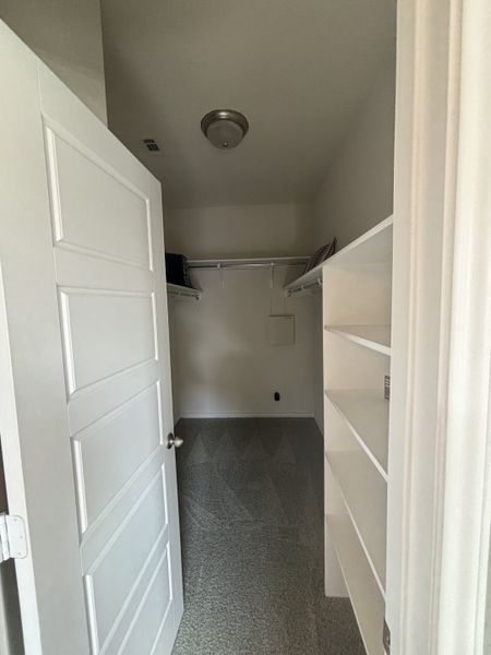 A spacious walk-in closet with built-in shelving and soft carpet, offering ample storage and functionality. A spacious walk-in closet with built-in shelving and soft carpet, offering ample storage and functionality.