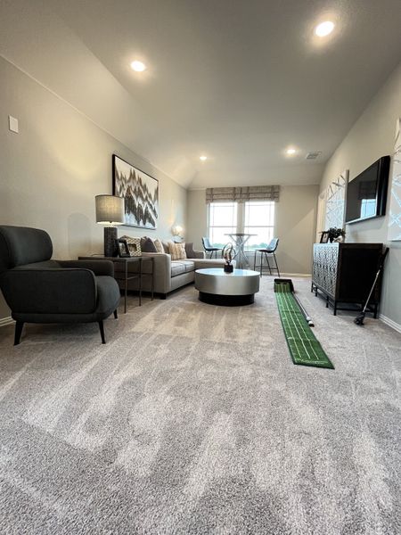 A cozy living room with plush carpeting, modern furniture, chic artwork, and a golf putting mat for practice.