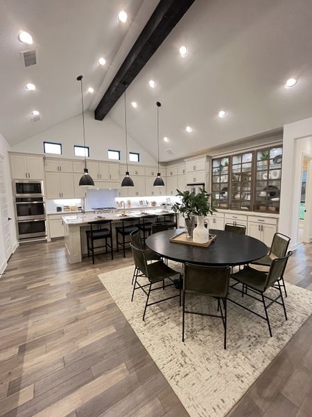 A spacious kitchen with vaulted ceilings, pendant lights, a large round table, and wood flooring.