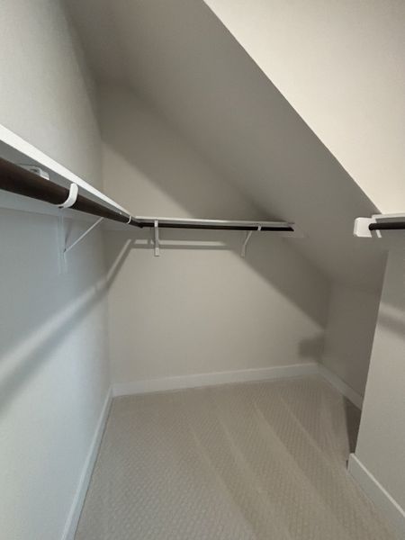 A cozy, angled walk-in closet with carpet flooring and dual hanging rods for ample storage.