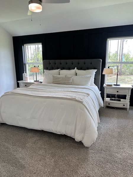 A cozy bedroom with a tufted headboard, plush carpeting, and large windows bringing in natural light.