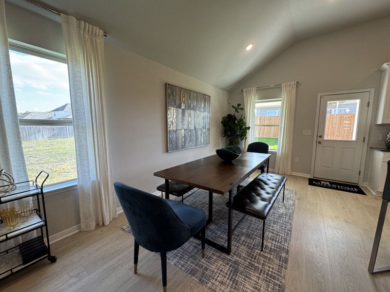 A bright dining area featuring a wooden table, blue chairs, a bench, and large windows with sheer curtains. A bright dining area featuring a wooden table, blue chairs, a bench, and large windows with sheer curtains.