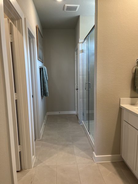 A modern bathroom featuring sleek tile flooring, a glass shower, and crisp white cabinetry.